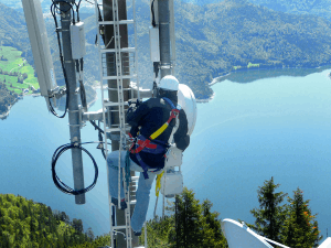Mann auf Mobilfunkmast vor See Telefonica